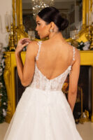 Back view of a model wearing an elegant white wedding gown with intricate floral lace appliqués, delicate embroidered straps, a deep V-back, and a flowing tulle ball gown skirt, set against a luxurious gold-accented interior.