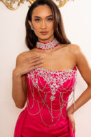 Model wearing a vibrant hot pink strapless gown with elaborate silver crystal embroidery, dangling rhinestone chains, and a matching embellished choker necklace.