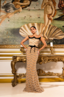 Model posing confidently in a strapless champagne-colored evening gown with black velvet accents and cascading crystal bead embellishments, standing before Botticelli's *The Birth of Venus* painting in an opulent interior.