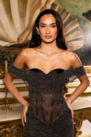 Model wearing a glamorous off-the-shoulder black mini dress fully embellished with iridescent multicolored crystals, featuring a sweetheart neckline and sheer mesh panels, posed confidently in an ornate interior.