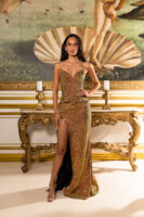 Model wearing a strapless, fully sequined bronze-gold evening gown with a structured sweetheart neckline corset top, peplum detail, and high-side-slit mermaid skirt, posed in an opulent interior with classical artwork backdrop.