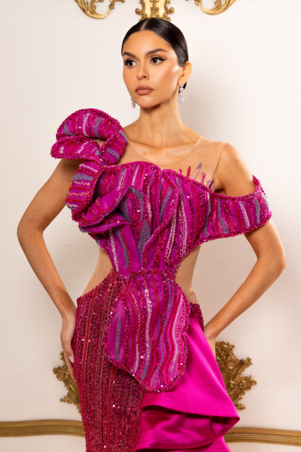 Model wearing a glamorous fuchsia evening gown with intricate sequin and bead embellishments in vertical stripes, featuring dramatic oversized ruffled shoulders, sheer illusion cutouts, and an asymmetrical peplum detail.