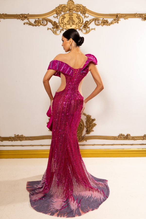 Model wearing a glamorous off-the-shoulder magenta sequin gown with ruffled sleeves, sheer side cutouts, lace-up back detailing, and a flowing train featuring a gradient feather-like pattern, viewed from behind.