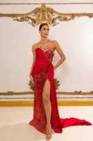 Elegant red strapless evening gown with intricate sequin and bead embellishments on a sheer overlay, featuring an asymmetrical draped sash, high side slit, and flowing train.
