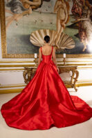 Model wearing a luxurious red satin ball gown with a fitted corset bodice, buttoned back, and voluminous train, viewed from behind in front of Botticelli's *The Birth of Venus* painting.