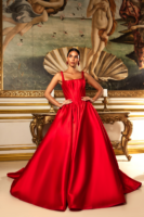 Model wearing an elegant, floor-length red satin ball gown with a fitted corset bodice, thick straps, and a voluminous skirt with train, posed confidently in front of a classical painting inspired by Botticelli's Birth of Venus.