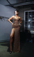 Strapless bronze sequined evening gown with sweetheart neckline, fitted bodice, and high side slit, modeled by a woman posing confidently with hands on hips.