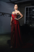 Elegant strapless red evening gown with intricate sequin and bead embellishments on the bodice, asymmetrical draped satin overlay, and high side slit, modeled in a dimly lit studio.